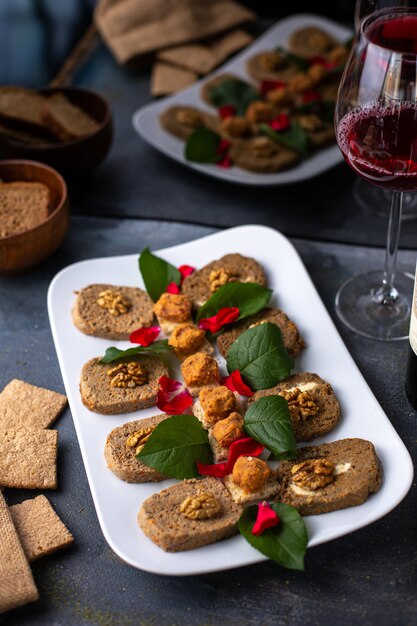 Un patè di verdure di vista frontale con le foglie verdi delle noci insieme ai prodotti del pasto del vino rosso delle patatine fritte sullo scrittorio grigio