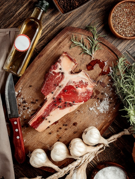 Un pezzo di carne per bistecca su una tavola di legno cosparsa di spezie