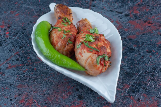 Un piatto bianco di cosce di pollo fritte con peperoncino.