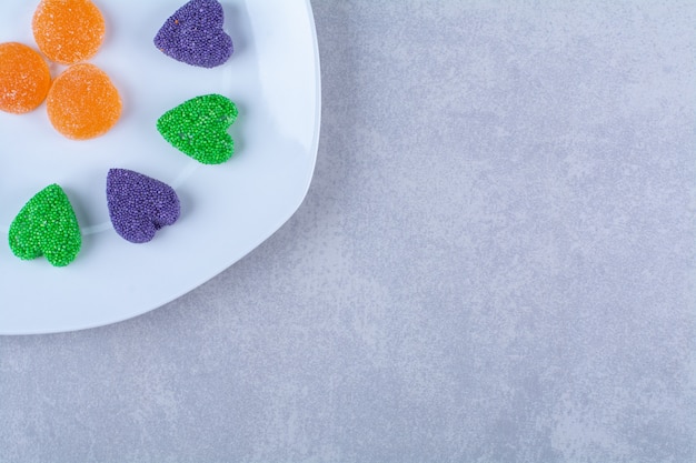 Un piatto bianco pieno di caramelle di gelatina zuccherate su sfondo grigio. Foto di alta qualità