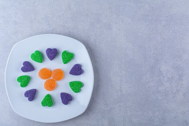 Un piatto bianco pieno di caramelle di gelatina zuccherate sul tavolo grigio.