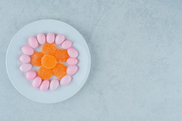 Un piatto bianco pieno di marmellate di arance dolci e caramelle rosa. Foto di alta qualità