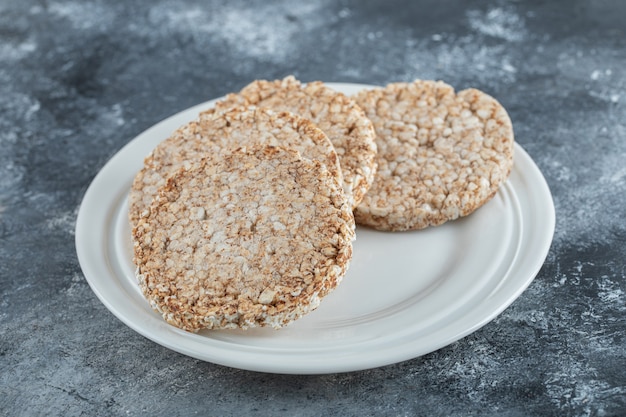 Un piatto bianco pieno di pane di riso soffiato su una superficie di marmo.