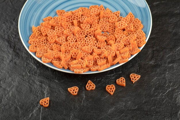 Un piatto blu con pasta cruda a forma di cuore sul tavolo nero