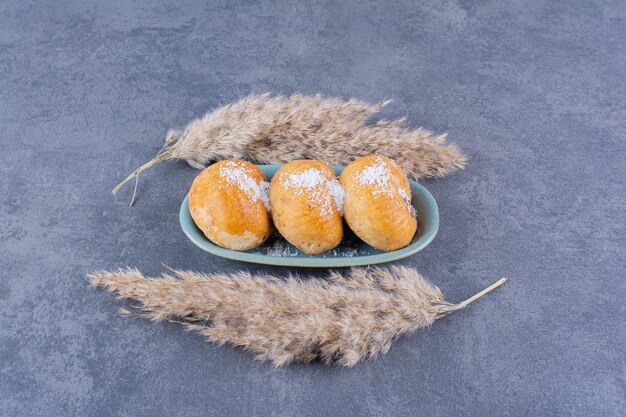 Un piatto blu di torte dolci con zucchero e spighe di grano su pietra.