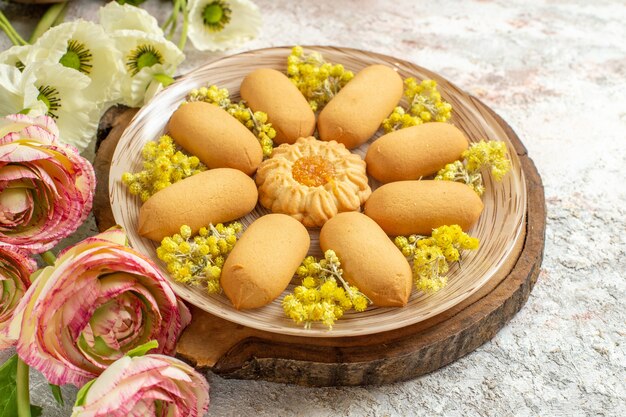 Un piatto di biscotti dolci su un vassoio di legno e bellissimi fiori colorati su fondo in marmo bianco