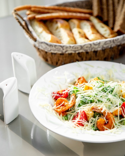 Un piatto di gamberi caesar salad servito con cesto di pane, sale e pepe