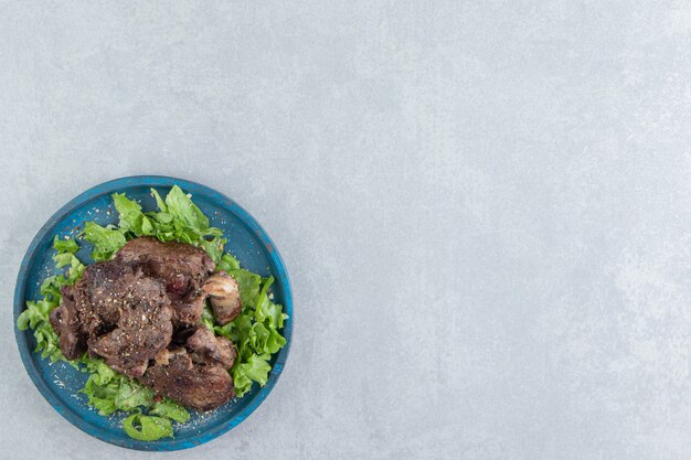 Un piatto di legno blu di carne fritta e lattuga affettata.