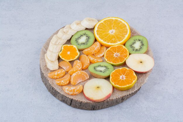 Un piatto di legno di frutta a fette su sfondo bianco. Foto di alta qualità