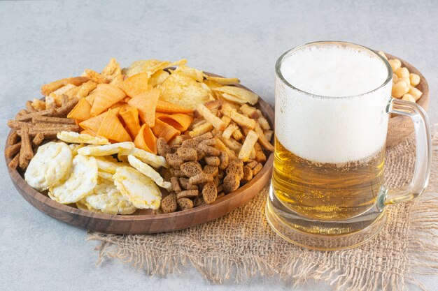 Un piatto di legno pieno di delizioso pesce e formaggio con birra e piselli.