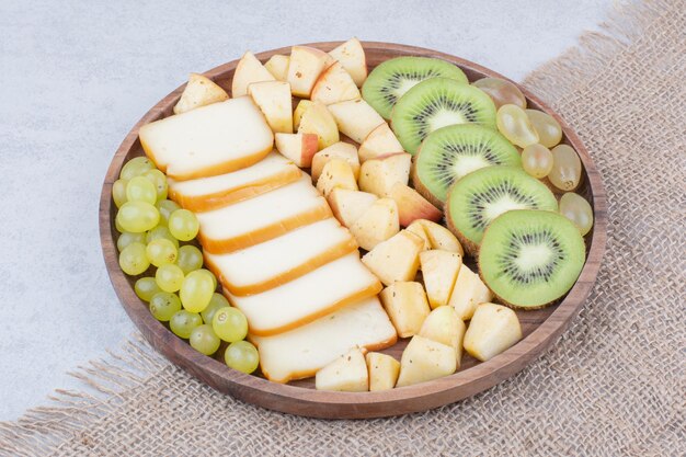 Un piatto di legno pieno di frutta a fette e pane. Foto di alta qualità