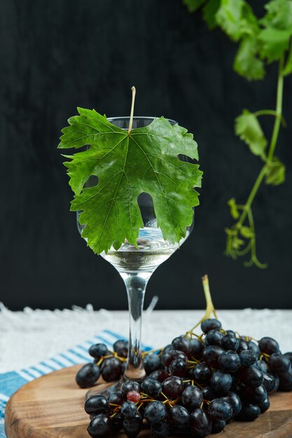 Un piatto di uva nera e un bicchiere di vino con foglia su sfondo scuro. Foto di alta qualità