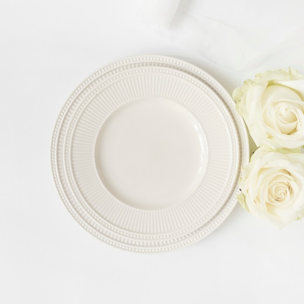 Un piatto e rose di ceramica vuoti su fondo bianco