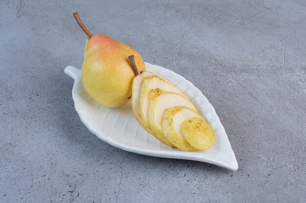 Un piatto fantasia con pera che serve su sfondo di marmo.