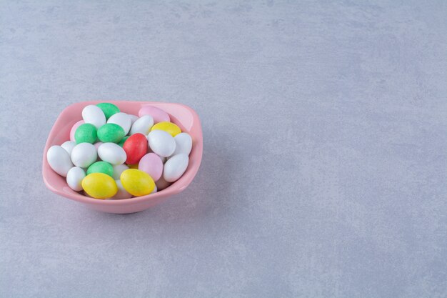 Un piatto fondo rosa pieno di caramelle colorate di fagioli su sfondo grigio. Foto di alta qualità