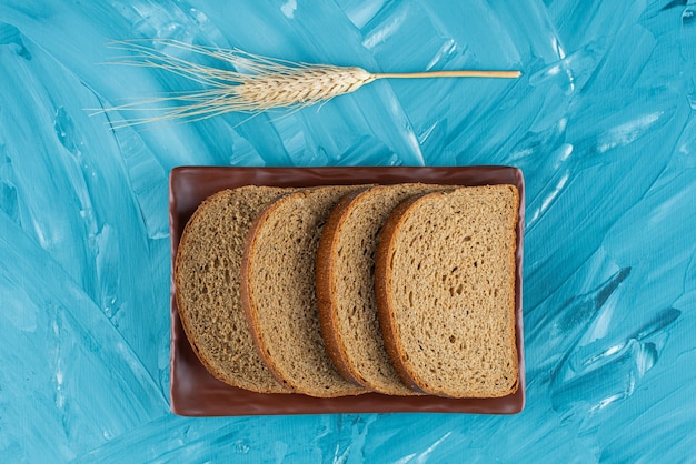 Un piatto marrone con pane a fette marrone e orecchio sulla superficie blu