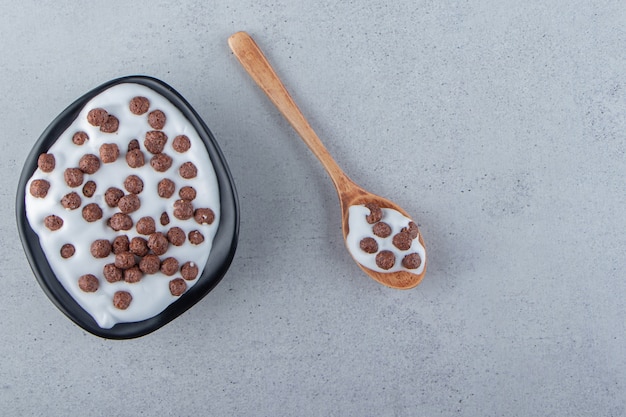 Un piatto nero profondo di latte con cereali al cioccolato e cucchiaio di legno. Foto di alta qualità