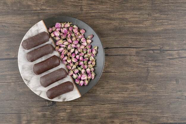 Un piatto pieno di crema al cioccolato rotoli con crema di latte con rose essiccate su un tavolo di legno.