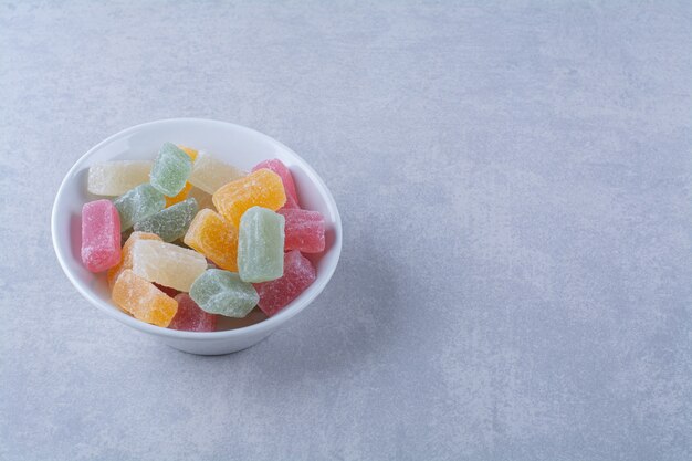 Un piatto profondo bianco pieno di caramelle colorate di fagioli su sfondo grigio. Foto di alta qualità