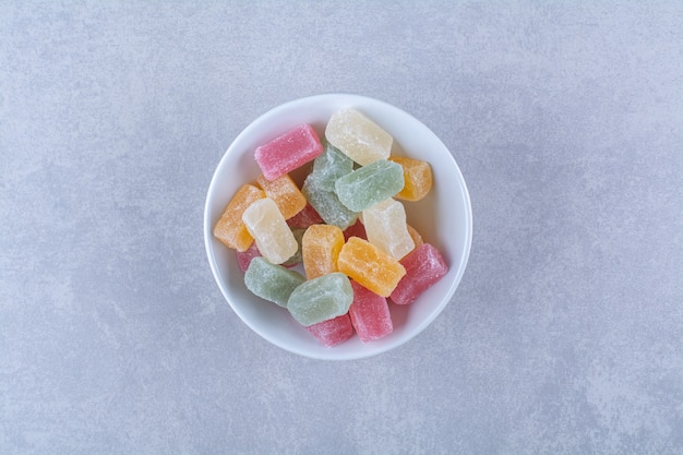 Un piatto profondo bianco pieno di caramelle colorate di fagioli su sfondo grigio. Foto di alta qualità