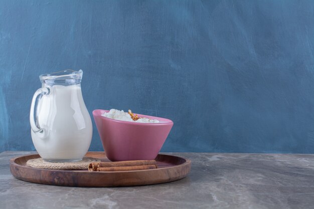 Un piatto rosa di porridge di farina d'avena sano con una brocca di vetro di latte e bastoncini di cannella su una tavola di legno.