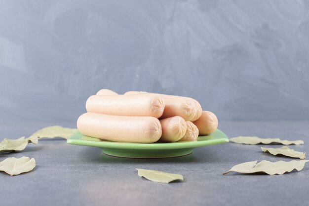 Un piatto verde con salsicce bollite e foglie di alloro