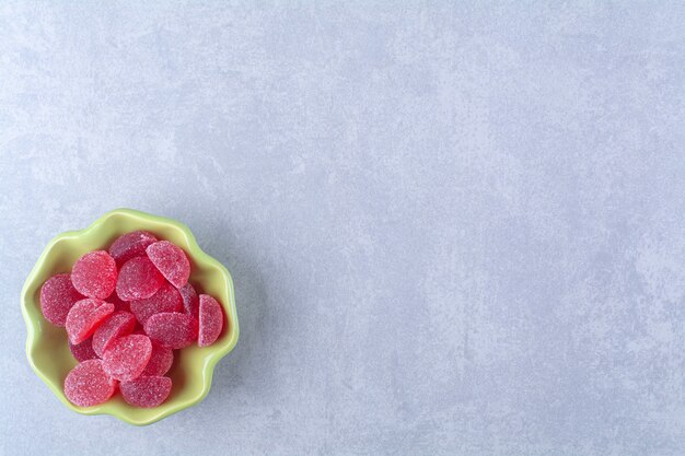 Un piatto verde pieno di caramelle di gelatina zuccherate sulla superficie grigia