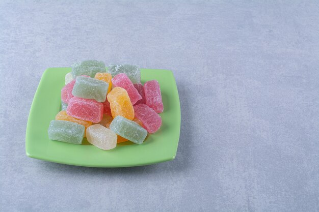 Un piatto verde pieno di caramelle di gelatina zuccherate sulla superficie grigia