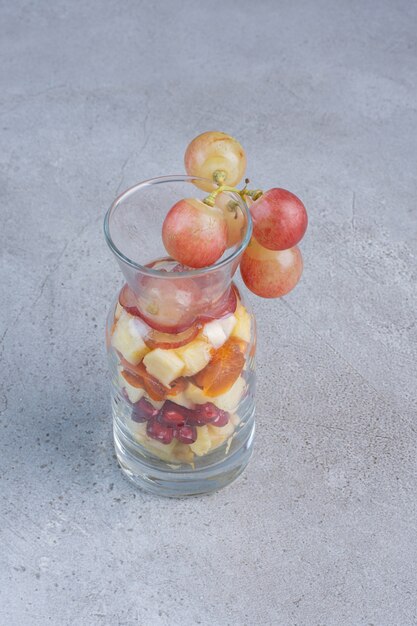 Un piccolo barattolo riempito con una varietà di frutta tritata su sfondo di marmo.