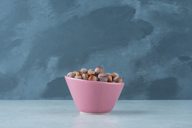 Un piccolo piatto rosa pieno di noci su sfondo marmo. Foto di alta qualità
