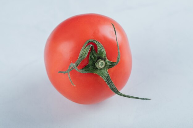 Un pomodoro fresco intero gustoso su una superficie bianca.