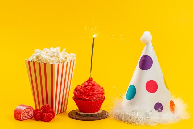 Un popcorn e una torta di vista frontale con protezione di compleanno e marmellate sullo scrittorio giallo