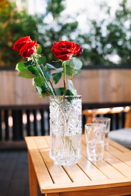 Un primo piano di tre belle rose rosse in vaso di vetro sopra la tavola di legno