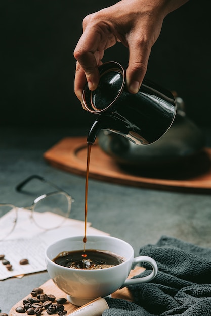 Un primo piano di una mano che versa l'acqua del caffè in una tazza di caffè, concetto di giornata internazionale del caffè