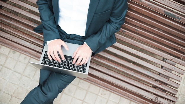 Un punto di vista elevato di un uomo d&#39;affari che si siede sul banco facendo uso del computer portatile