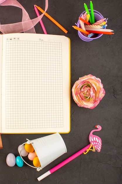 Un quaderno con vista dall'alto e un fiore con caramelle colorate e candele sul fiore della foto della caramella di colore scuro dello scrittorio