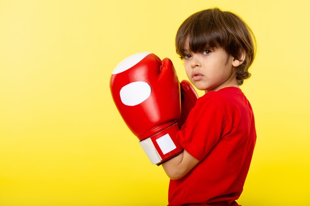 Un ragazzo carino vista frontale in guantoni da boxe rossi e maglietta rossa sul muro giallo