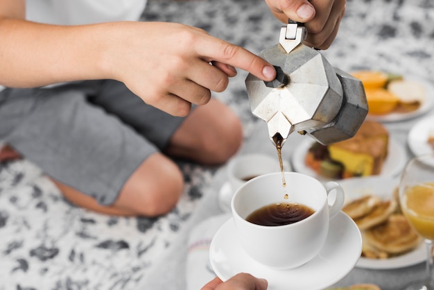 Un ragazzo che versa caffè nero in una tazza per l&#39;altra persona a colazione