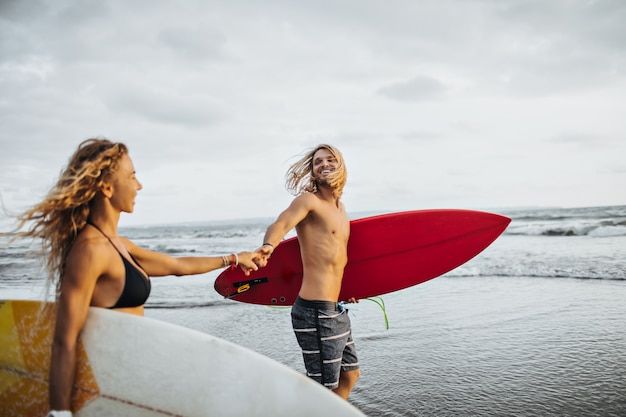 Un ragazzo e una ragazza gioiosi corrono in mare e tengono le tavole per il surf