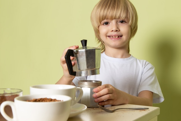 Un ragazzo sorridente felice di vista della fonte che prepara la bevanda del caffè sulla tavola sul pavimento colorato pietra