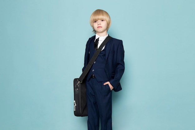 Un ragazzo sveglio di affari di vista frontale in vestito classico blu che indossa borsa nera che posa modo del lavoro di affari