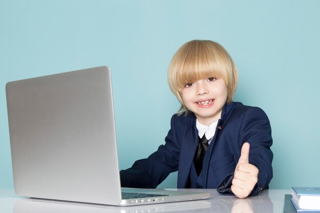 Un ragazzo sveglio di affari di vista frontale in vestito classico blu che posa davanti al computer portatile d'argento che lavora modo sorridente del lavoro di affari