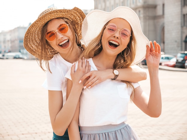 Un ritratto di due giovani belle ragazze sorridenti bionde dei pantaloni a vita bassa in vestiti bianchi della maglietta dell'estate d'avanguardia.