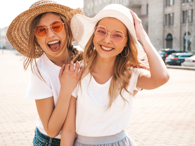 Un ritratto di due giovani belle ragazze sorridenti bionde dei pantaloni a vita bassa in vestiti bianchi della maglietta dell'estate d'avanguardia.