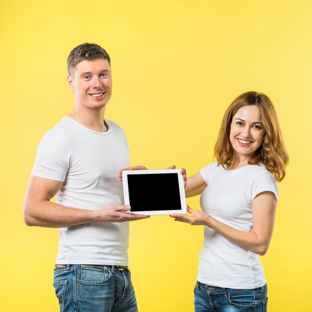 Un ritratto di due giovani coppie felici che mostrano compressa digitale dello schermo nero contro il contesto giallo