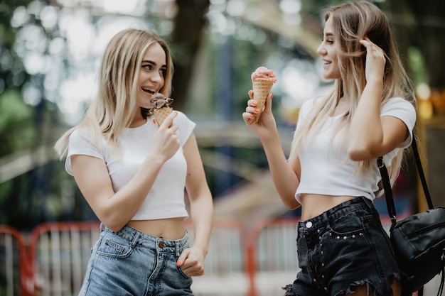 Un ritratto di due ragazze in vetri che leccano il gelato nel parco della città