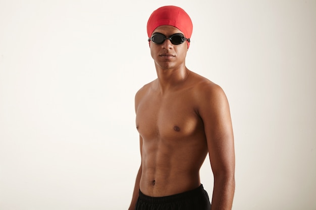 Un ritratto di un nuotatore olimpico in forma che indossa berretto rosso e occhiali di protezione neri su fondo bianco