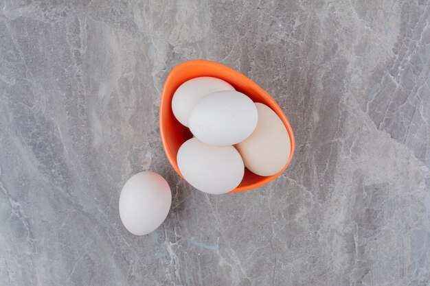 Un sacco di uova bianche di pollo fresco su un piatto arancione. Foto di alta qualità