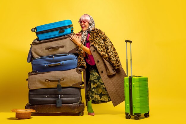 Un sacco di vestiti per viaggiare. Ritratto di donna caucasica su sfondo giallo. Bellissima modella bionda.