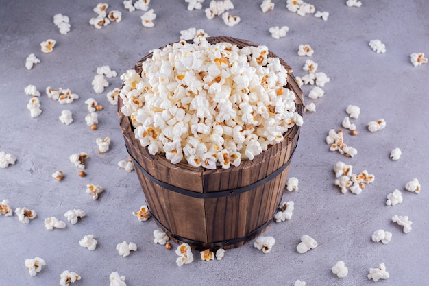 Un secchio di legno troppo pieno nel mezzo di popcorn sparsi su uno sfondo di marmo. Foto di alta qualità